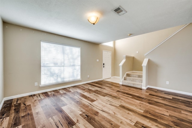 unfurnished living room with stairway, wood finished floors, visible vents, and baseboards