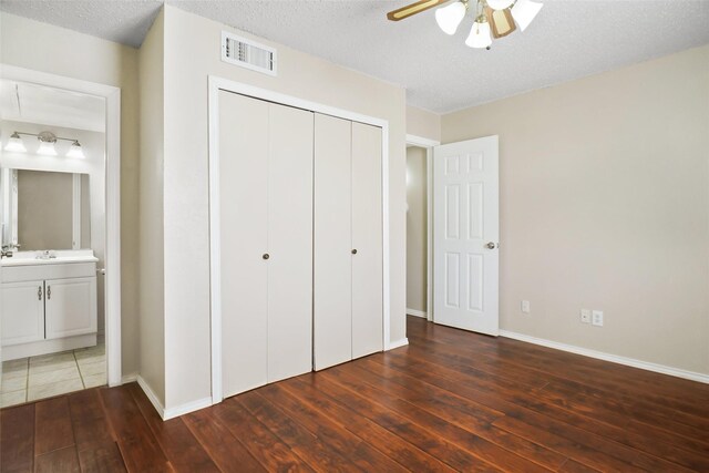 unfurnished bedroom with baseboards, a closet, ensuite bath, visible vents, and hardwood / wood-style floors