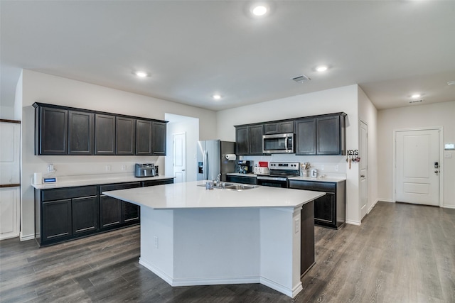 kitchen with dark wood-type flooring, an island with sink, a sink, appliances with stainless steel finishes, and light countertops