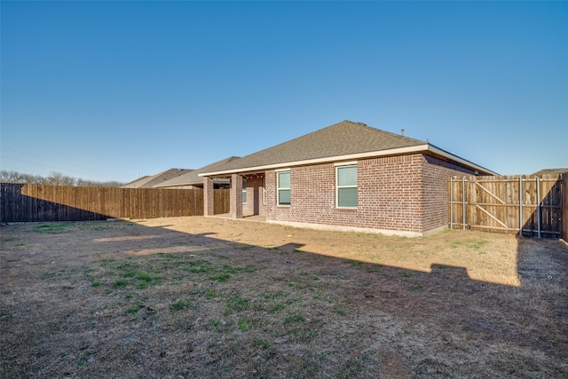 back of property with brick siding, roof with shingles, and a fenced backyard