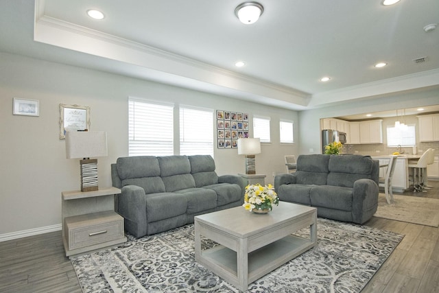 living area with light wood finished floors, visible vents, baseboards, a tray ceiling, and ornamental molding