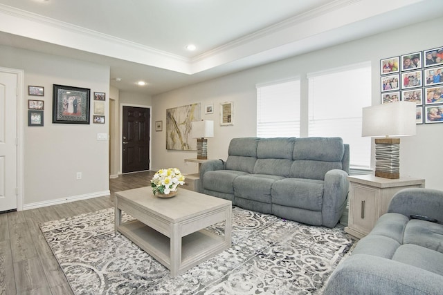 living room featuring crown molding, baseboards, recessed lighting, light wood-style flooring, and a raised ceiling