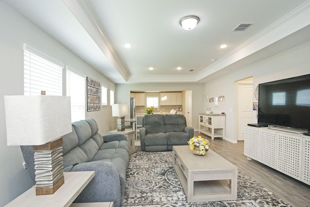 living room featuring wood finished floors, visible vents, a tray ceiling, recessed lighting, and ornamental molding