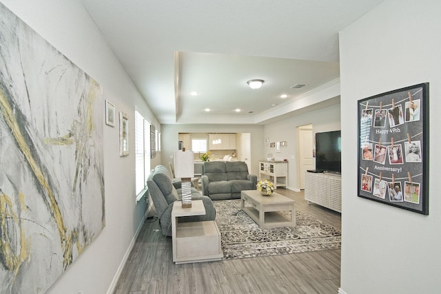 living room with visible vents, baseboards, a tray ceiling, and wood finished floors