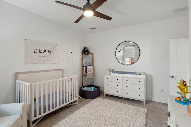 bedroom with visible vents, a crib, carpet flooring, baseboards, and ceiling fan