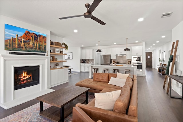 living room with visible vents, dark wood-type flooring, a glass covered fireplace, recessed lighting, and ceiling fan