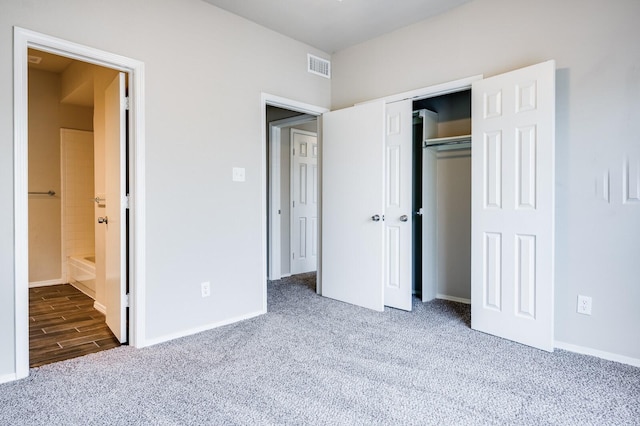 unfurnished bedroom featuring visible vents, ensuite bath, a closet, carpet flooring, and baseboards