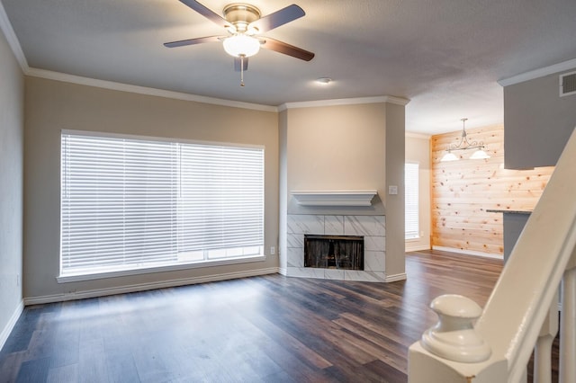 living room featuring wooden walls, a ceiling fan, dark wood-style floors, ornamental molding, and a tiled fireplace