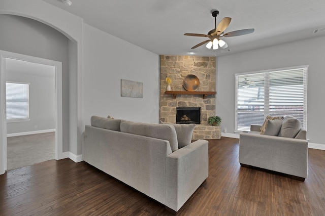 living room with baseboards, plenty of natural light, dark wood-type flooring, and a stone fireplace