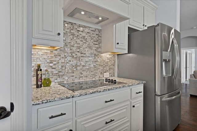 kitchen featuring backsplash, premium range hood, stainless steel refrigerator with ice dispenser, white cabinetry, and black electric cooktop