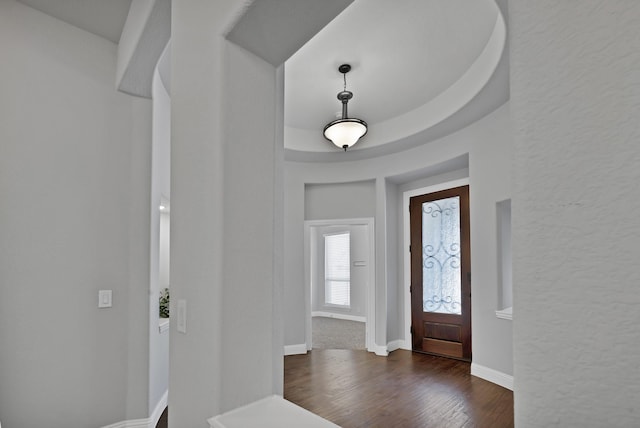 foyer entrance featuring a textured wall, a raised ceiling, baseboards, and dark wood-style flooring