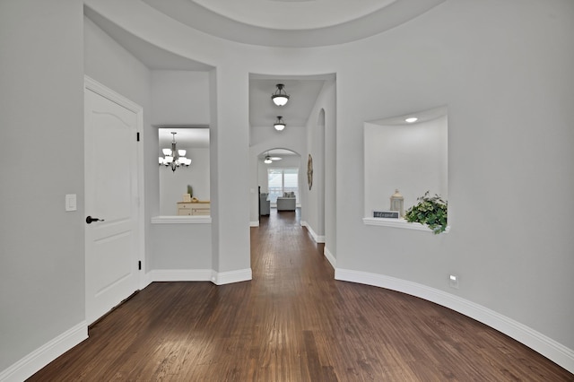 hall featuring baseboards, arched walkways, and dark wood-type flooring