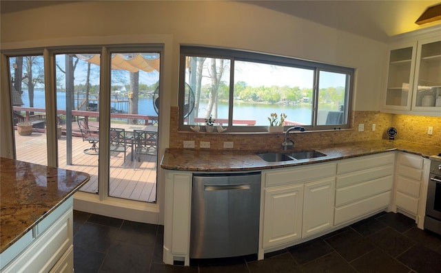 kitchen featuring backsplash, appliances with stainless steel finishes, a sink, dark stone countertops, and glass insert cabinets