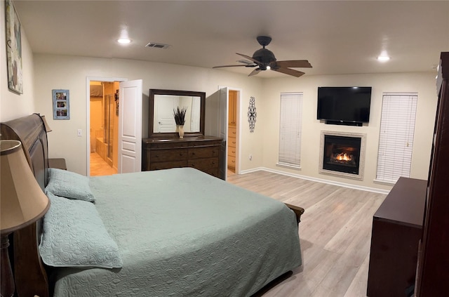 bedroom featuring visible vents, wood finished floors, baseboards, a glass covered fireplace, and recessed lighting