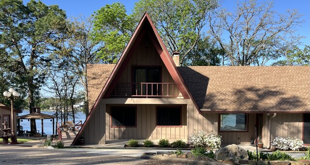 view of front of home featuring a balcony, a chimney, a shingled roof, board and batten siding, and a gazebo