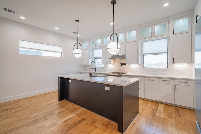 kitchen featuring tasteful backsplash, white cabinets, light wood-style floors, and a sink