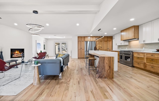 kitchen featuring light wood-style flooring, backsplash, open floor plan, a lit fireplace, and appliances with stainless steel finishes