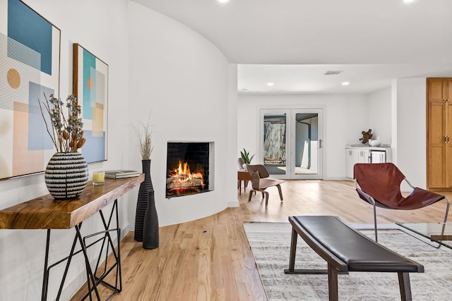 living room with visible vents, recessed lighting, a warm lit fireplace, light wood-style floors, and french doors