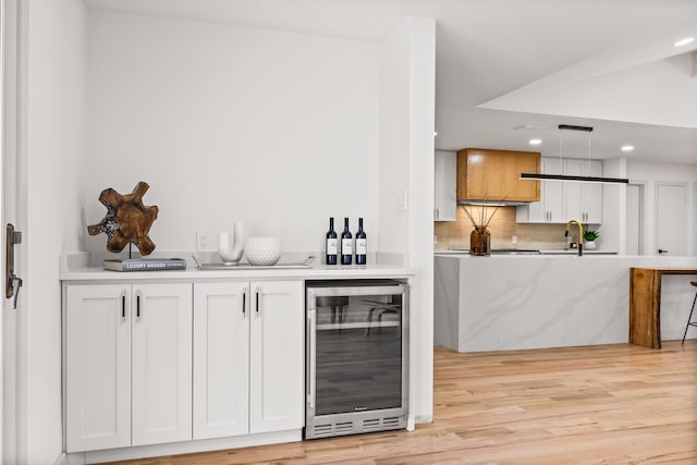 bar featuring light wood-type flooring, beverage cooler, a sink, backsplash, and recessed lighting