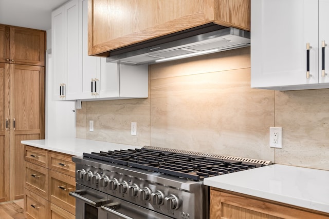 kitchen with double oven range, light countertops, white cabinetry, wall chimney exhaust hood, and tasteful backsplash