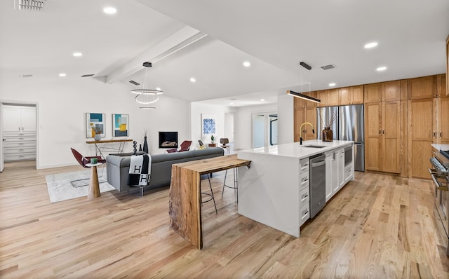 kitchen featuring a center island with sink, stainless steel appliances, a sink, light countertops, and light wood-type flooring