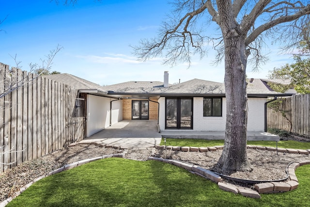 back of house with a patio, roof with shingles, a yard, a fenced backyard, and brick siding