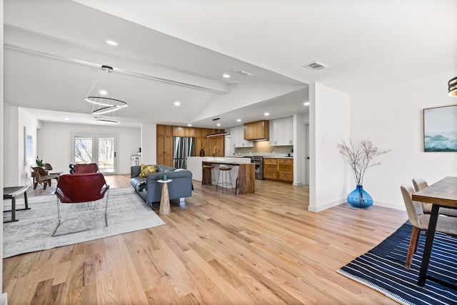 living room featuring light wood finished floors, visible vents, lofted ceiling with beams, and baseboards