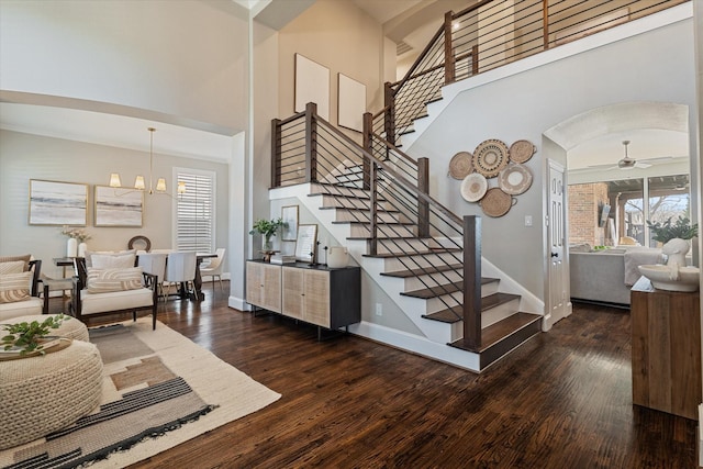 staircase with ceiling fan with notable chandelier, wood finished floors, arched walkways, baseboards, and a towering ceiling