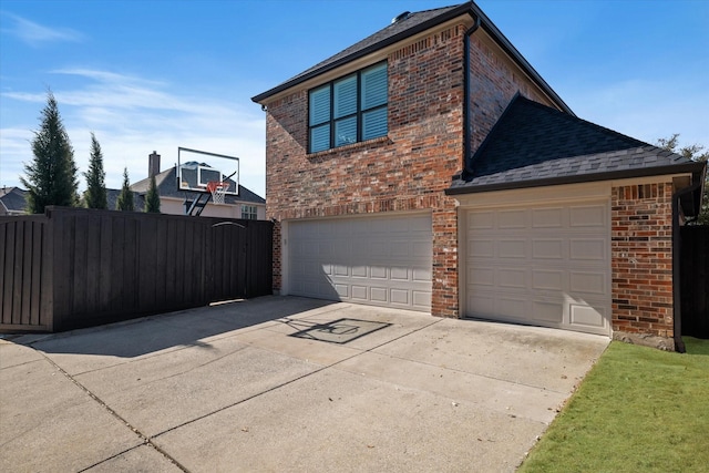 view of side of home featuring brick siding, an attached garage, driveway, and fence