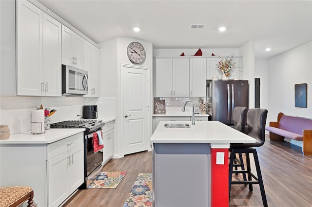 kitchen with an island with sink, a sink, a kitchen breakfast bar, wood finished floors, and stainless steel appliances