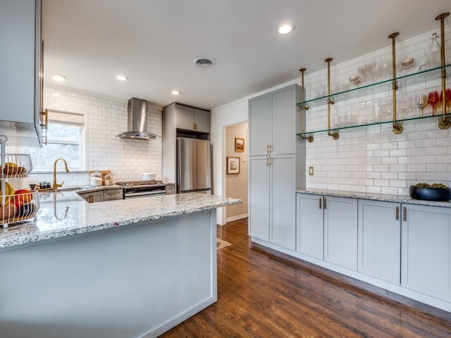 kitchen featuring light stone countertops, gray cabinets, a sink, appliances with stainless steel finishes, and wall chimney range hood