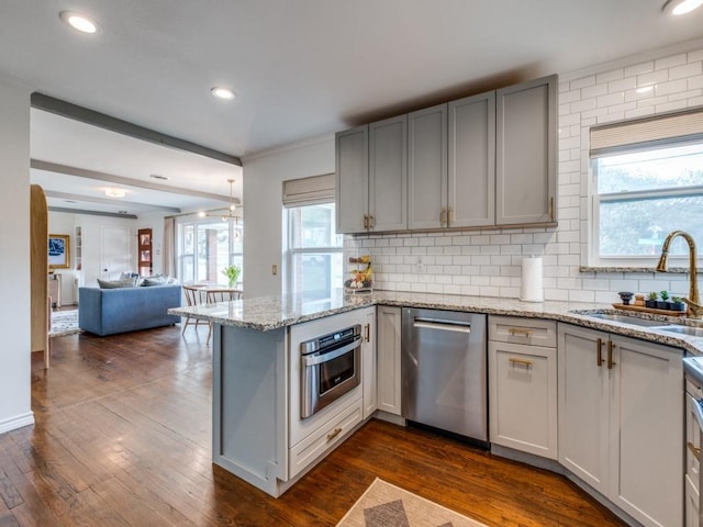 kitchen with a peninsula, dark wood-style floors, stainless steel appliances, and a sink