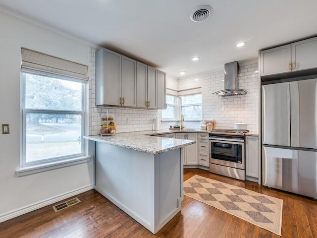 kitchen with visible vents, a peninsula, dark wood-style flooring, stainless steel appliances, and wall chimney range hood