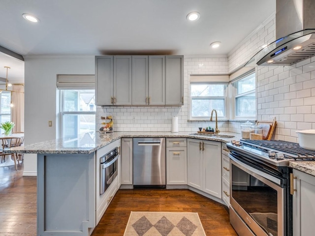 kitchen featuring dark wood finished floors, a peninsula, a sink, stainless steel appliances, and wall chimney range hood