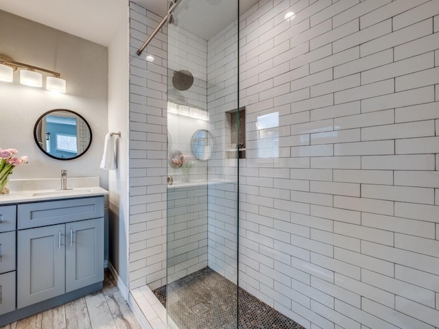 bathroom with a tile shower, vanity, and wood finished floors