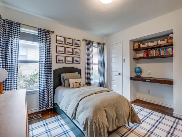 bedroom with multiple windows, wood finished floors, visible vents, and built in study area