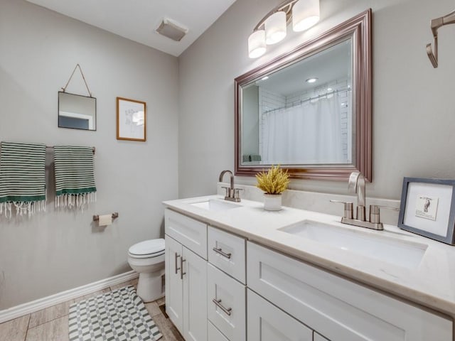 bathroom featuring double vanity, toilet, baseboards, and a sink