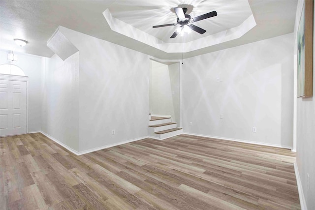 empty room with stairs, a raised ceiling, baseboards, and wood finished floors