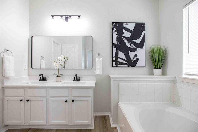 bathroom with double vanity, wood finished floors, a garden tub, and a sink