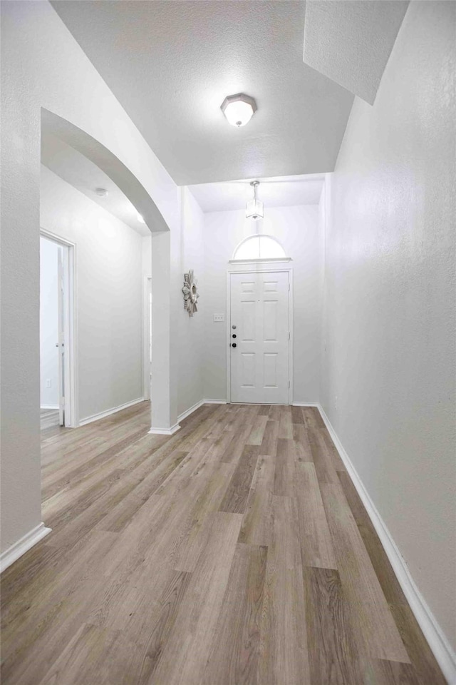 interior space with baseboards, arched walkways, and wood finished floors