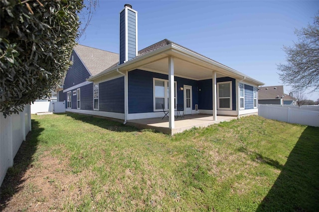 back of house featuring a yard, a patio, a fenced backyard, and a chimney