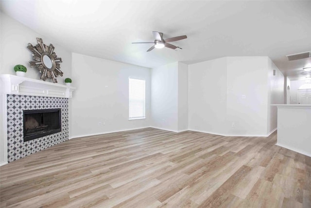 unfurnished living room with a tiled fireplace, light wood-style floors, visible vents, and ceiling fan