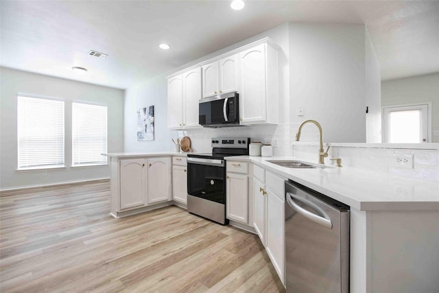 kitchen featuring a sink, backsplash, a peninsula, appliances with stainless steel finishes, and light wood finished floors