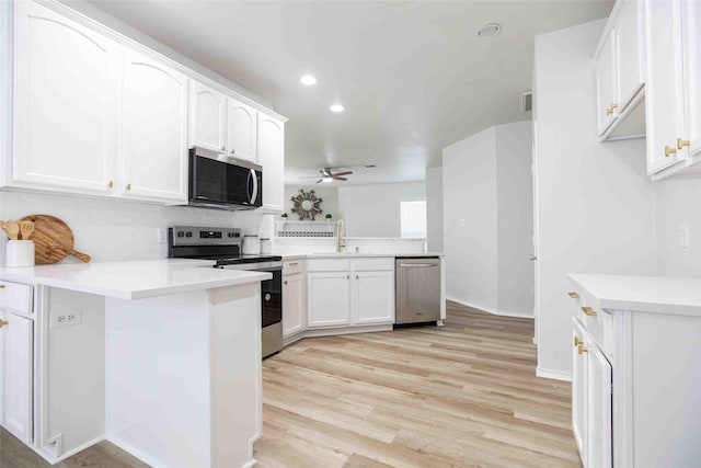 kitchen with a sink, white cabinetry, light wood-style floors, appliances with stainless steel finishes, and a peninsula