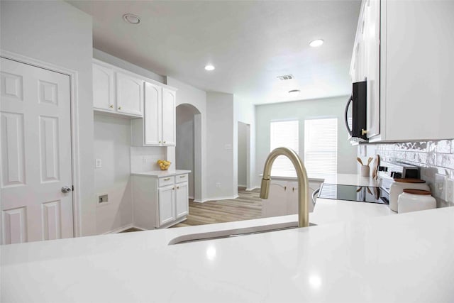 kitchen with a sink, backsplash, white cabinets, and black microwave