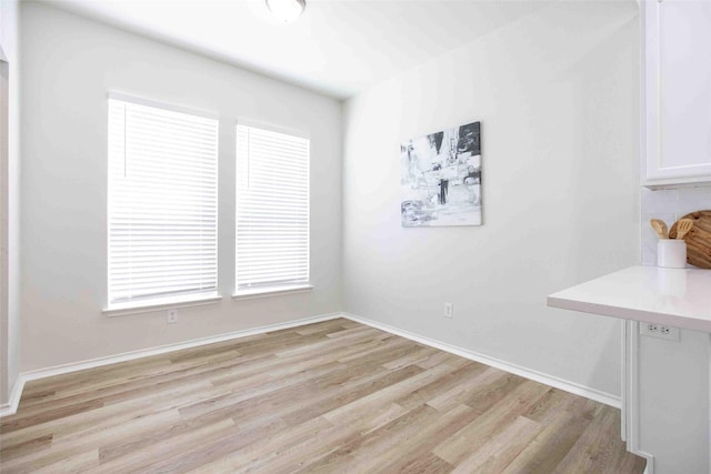 unfurnished dining area featuring baseboards and light wood-type flooring