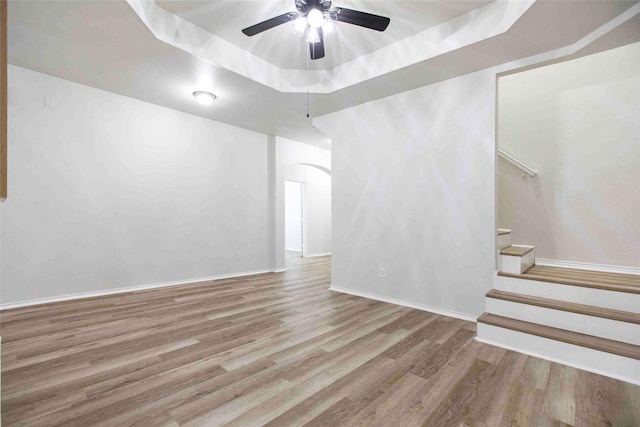 empty room featuring wood finished floors, baseboards, a tray ceiling, arched walkways, and stairs