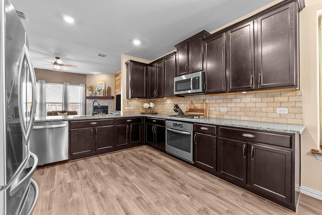 kitchen featuring light wood finished floors, light stone countertops, decorative backsplash, stainless steel appliances, and a sink