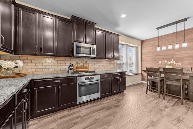 kitchen with tasteful backsplash, light stone countertops, dark brown cabinetry, light wood-style flooring, and appliances with stainless steel finishes