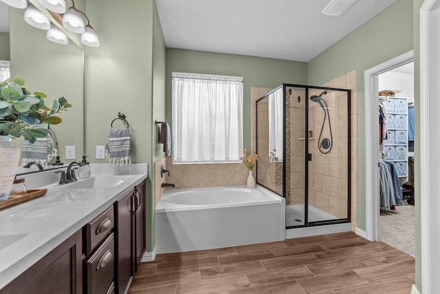 bathroom featuring wood finish floors, a sink, a shower stall, double vanity, and a bath